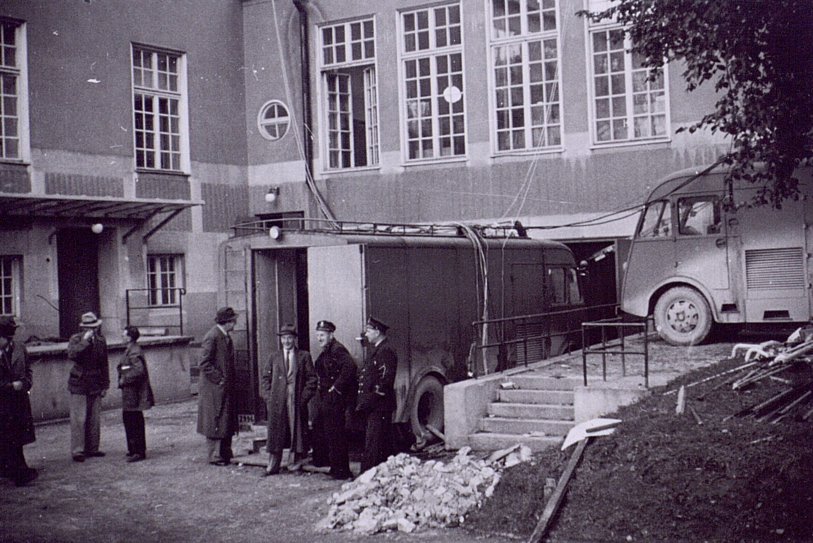 Schwarzweißfoto von 1942: ein Omnibus mit Kastenaufbau steht dicht an einem Gebäude, Kabel laufen zu den Fenstern, davor stehen mehrere Männer