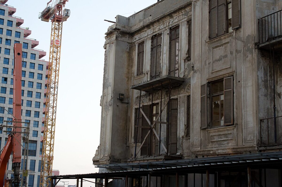 Baukran und Abbruchbagger neben einer verfallenen Fassade